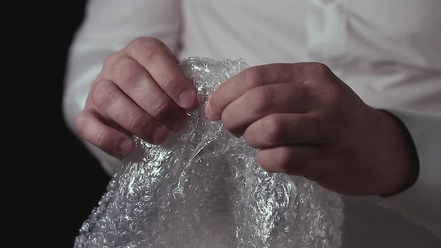 Male hands popping the bubbles in bubble wrap to relieve stress. Soothing therapy for nervousness or just for fun.