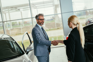 car sell agent handshake with client in car showroom