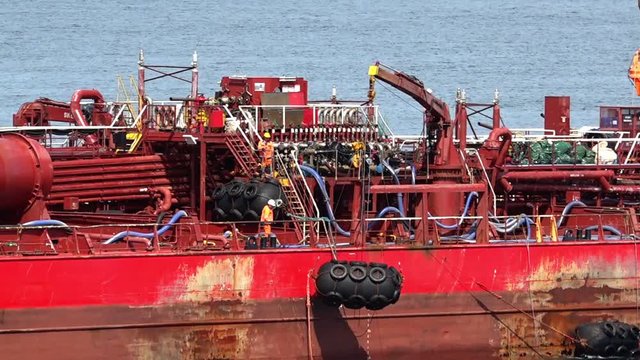 Red Oil Tanker Crane Puts Black Air Barrel Down On Blue Sea Water From Upper Deck On Sunny Day