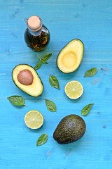 Top table dish with natural avocado, olive oil, limes and mint leaves on blue background. Vertical.