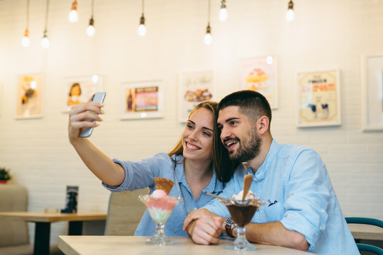 happy couple eating ice cream and using cellphone indoor