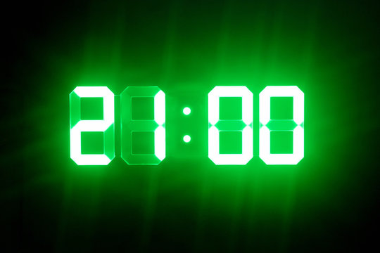 Green glowing digital clocks in the dark show 21:00 time