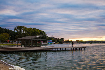 Naklejka premium A lonely girl stands on the pier and admires the beautiful sunset