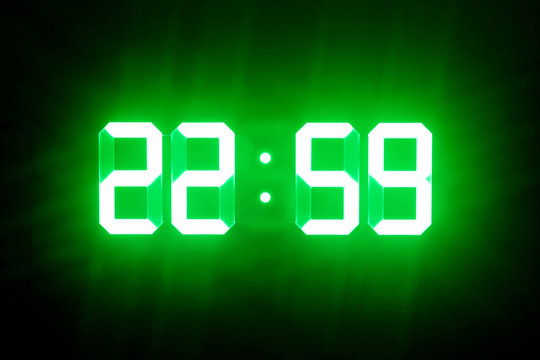 Green glowing digital clocks in the dark show 22:59 time