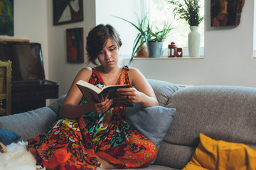 woman relaxed in sofa reading book with her dog