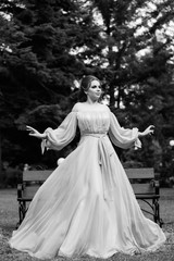 Fototapeta na wymiar Fashion photo of beautiful woman with in elegant dress. Woman in long flying evening dress. Elegant hairstyle and makeup. Black and white. 