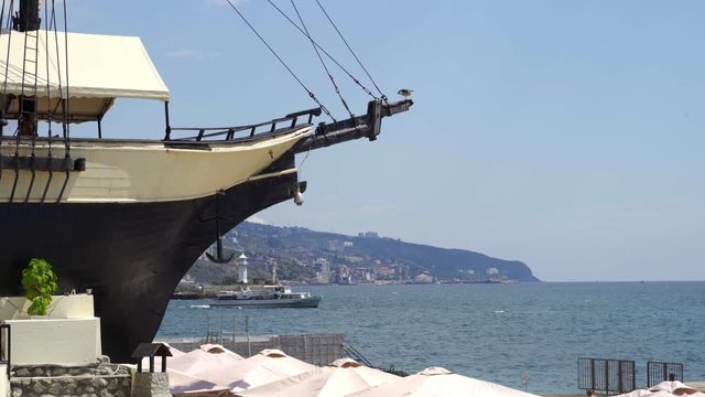 The nose of the old ship against the backdrop of the sea lighthouse and a passing passenger boat. A seagull sits on the bowsprit 4k
