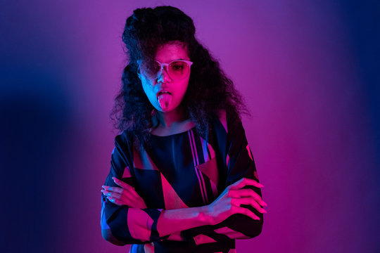 Naughty fashion young african american girl black woman wear stylish pink glasses arms crossed show tongue look at camera isolated on party purple studio background, portrait, copy space
