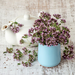 Fresh flowering oregano grass (Origanum vulgare) and a small teapot on the old table. Selective focus.