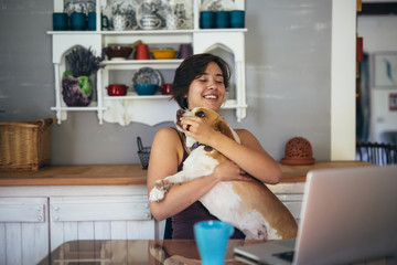 woman holding her dog in lap and using laptop at home