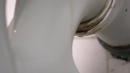 Leaking water from a toilet due to pipe blockage or worn out parts. Smelly water drops dropping behind the toilet from dirty pipe. Toilet leakage, bad smell, plumber needs to take care of it
