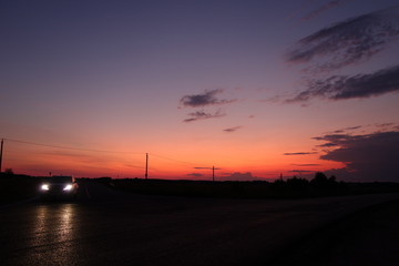Sunset noir in red and orange with car headlights reflected on tarmac in black foreground