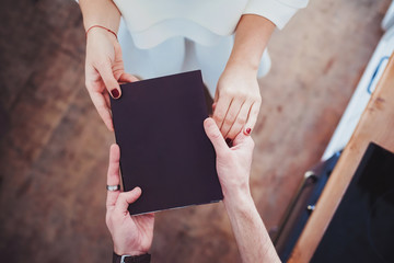 Male and female hands holding a book in a black cover. Relationship, gift.Copy space.