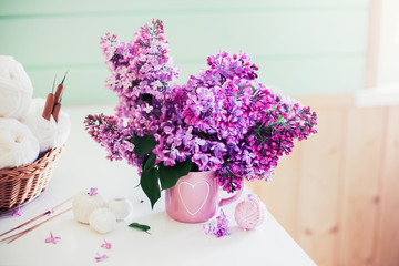 Crochet and knitting. Women's working space. Bouquet of lilac, yarn, crochet hooks on the white dresser in the mint wooden room. Favorite hobby.