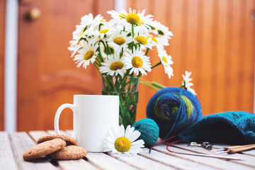 Women's hobby. Crochet and knitting. Workspace. A bouquet of daisies in a vase, a white Cup with a...