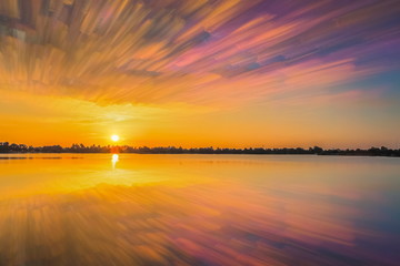 Obraz premium Lake view morning of Lotus lake with yellow sun light and clouds moving in the sky background (with clouds stack graphic), sunrise at Krajub Reservoir, Ban Pong District, Ratchaburi, Thailand.
