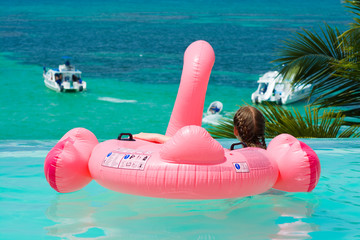Caucasian teenager girl with inflatable flamingo relaxing in infinity swimming pool in luxury hotel looking at the view, Punta Cana, Dominican Republic. Summer vacation concept - obrazy, fototapety, plakaty