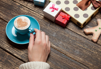 Female holding cup of coffee on wooden table near christmas gifts