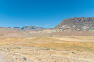 Panoramic view on the yellow field with dry grass and rock and mountains.