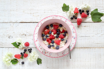A bowl of cottage cheese with raspberries and blueberries on a white wooden table, flat lay style