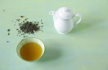 green tea in a bowl with a teapot and loose tea on a light green surface. It is a rich source of antioxidants and polyphenols. A healthy drink for health and vitality. Top view.