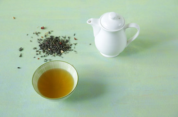 green tea in a bowl with a teapot and loose tea on a light green surface. It is a rich source of antioxidants and polyphenols. A healthy drink for health and vitality. Top view.
