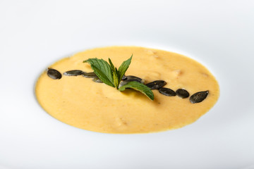 pumpkin cream soup in a white plate. On a soup are beans pumpkin and basil leaves.