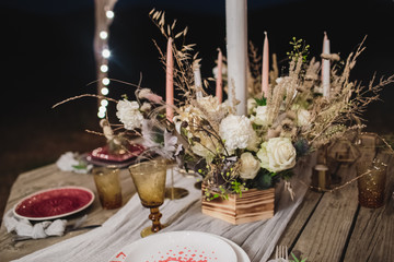 Romantic dinner on a wooden table with burgundy plates and fresh flowers. 