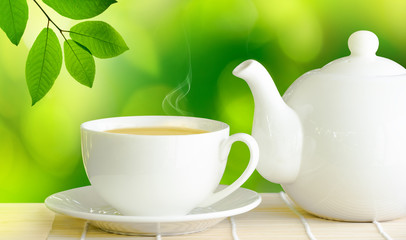 Cup of green tea and white ceramic teapot on wooden table.