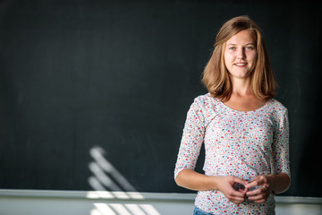 Pretty, young female student/young teacxher in front of a blackboard during class