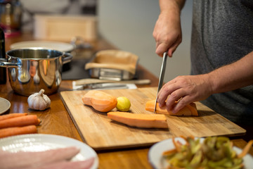 Mann schneidet mit Küchenmesser auf Holz-Schneidebrett eine Süsskartoffel, Nahaufnahme Hände