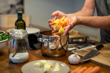 Würfel aus Süsskartoffel und Kartoffel fallen von Händen eines Mannes in den Kochtopf, Nahaufnahme