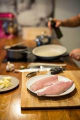 rohe Fisch Filets auf Teller in der Küche, dahinter unscharf Herd, Pfanne, Hände eines Mannes, Ölflasche