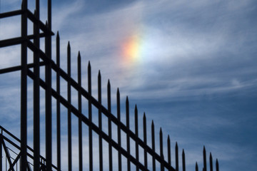 Silhouette of a fence with blue sky and rainbow