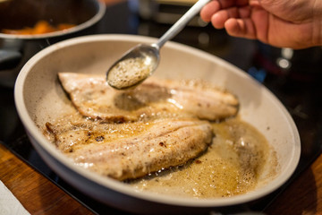 Koch schwenkt und übergießt Fisch Filet in Pfanne mit heißer Butter, Nahaufnahme