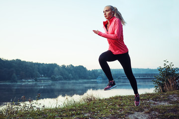 Athletic woman doing sprinting and jumping exercises during morning workout on autumn day