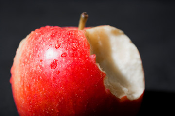 Manzana roja mordida con gotas de agua sobre fondo negro.