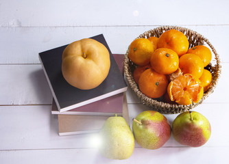 Gruop of orange fruit put in woven basket,beside blurred Chinese pear,on timber board