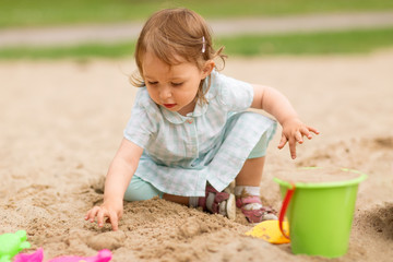 childhood, leisure and people concept - little baby girl plays with toys in sandbox