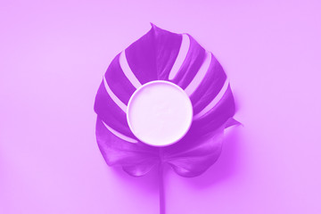 Moisturizing skin care cream on monstera leaf over trendy violet neon color background with copy...