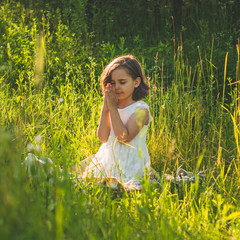 Little Girl closed her eyes, praying in a field during beautiful sunset. Hands folded in prayer...