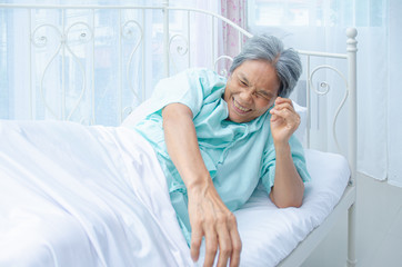 An old Asian woman wearing a green shirt Sleeping on the bed in the room. Elderly people are not comfortable. Women have white hair on their heads.