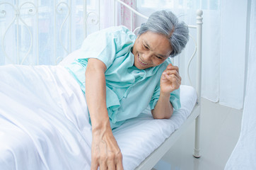 An old Asian woman wearing a green shirt Sleeping on the bed in the room. Elderly people are not comfortable. Women have white hair on their heads.