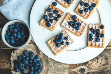 a plate with waffles, dusted with powdered sugar and fresh blueberries