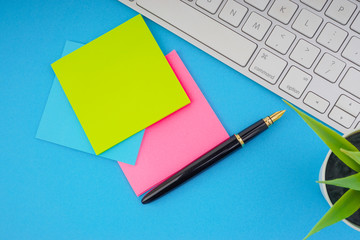 Flat lay, top view office table desk. Workspace with pen, sticky notes, decoration vase and keyboard on the blue background. Business Finance, Education and Copy Space concept