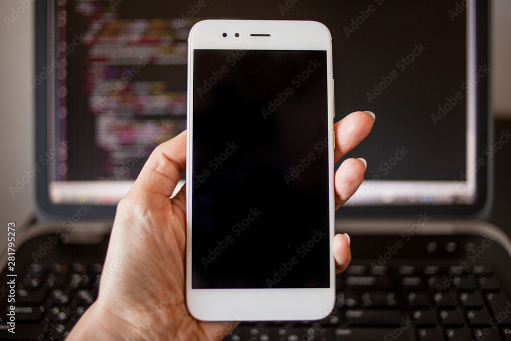Poster smartphone in hand on the background of the programmer's laptop.