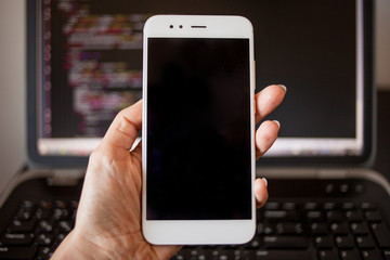 Smartphone in hand on the background of the programmer's laptop.