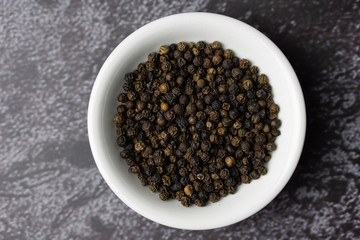 Black pepper in a bowl on dark background.