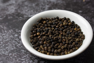 Black pepper in a bowl on dark background.