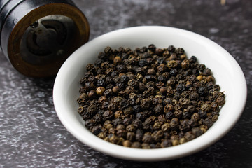 Black pepper in a bowl on dark background.
